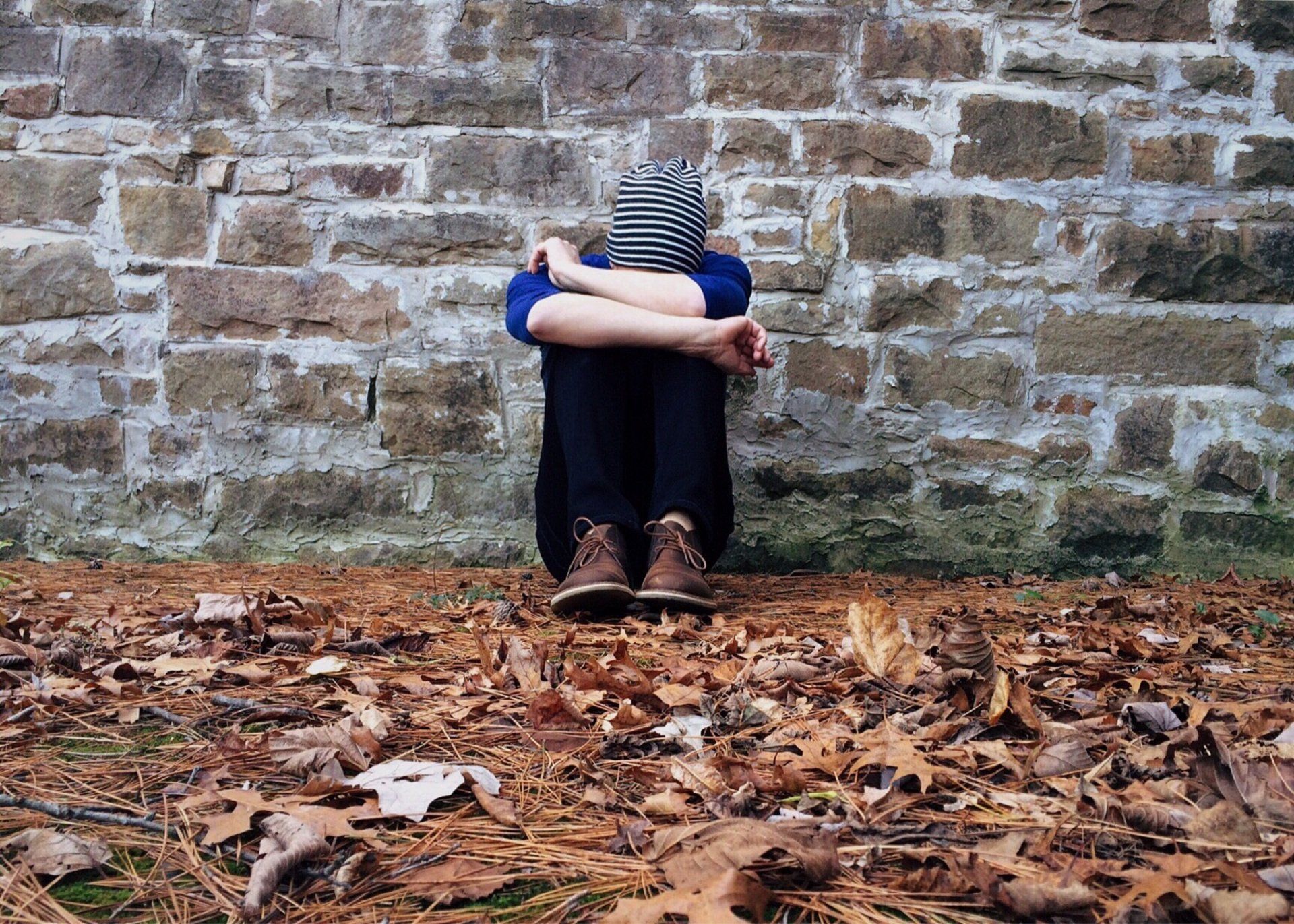a young person is sitting in front of a brick wall with his head down who is depressed