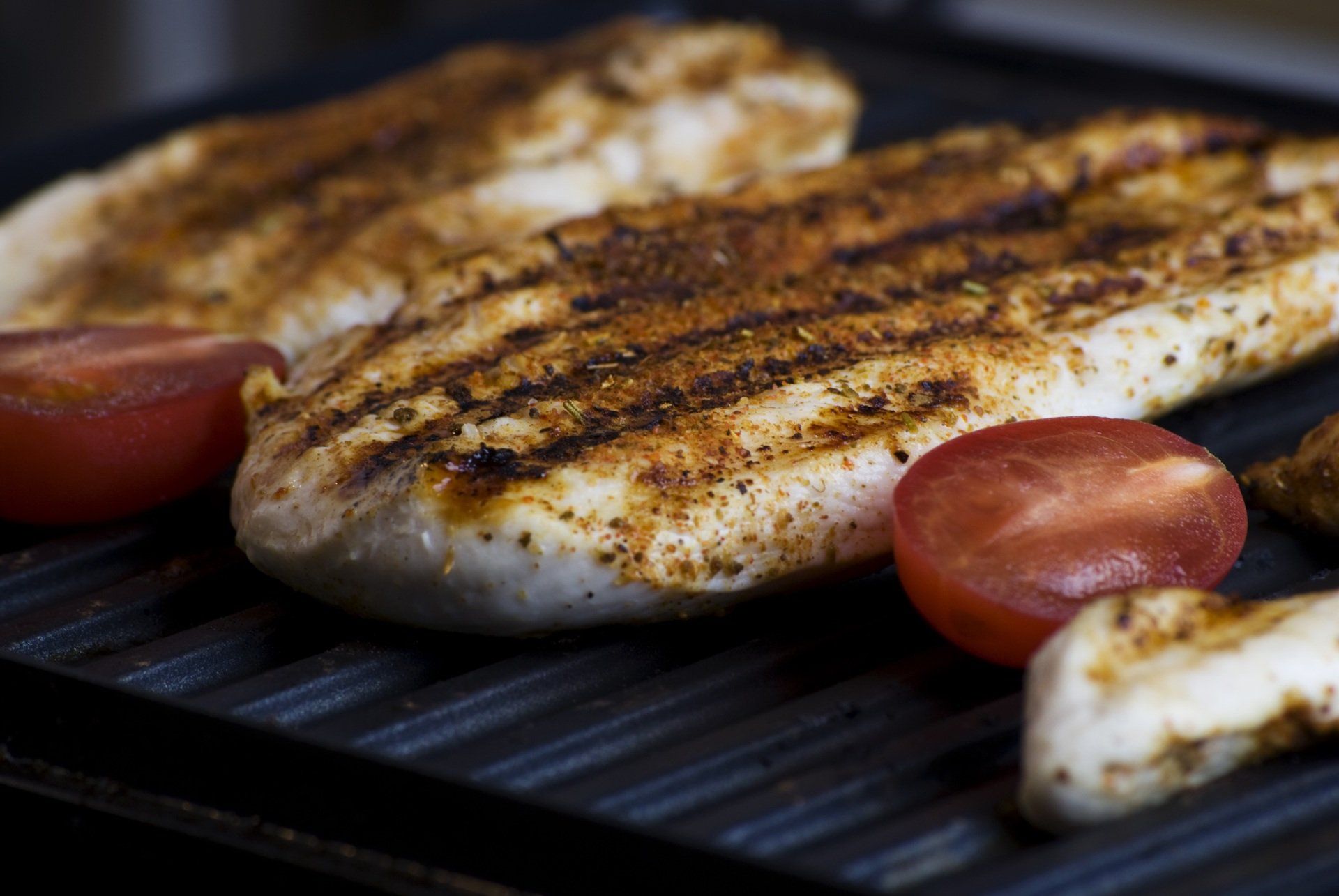 Chicken breasts and tomatoes are cooking on a grill.
