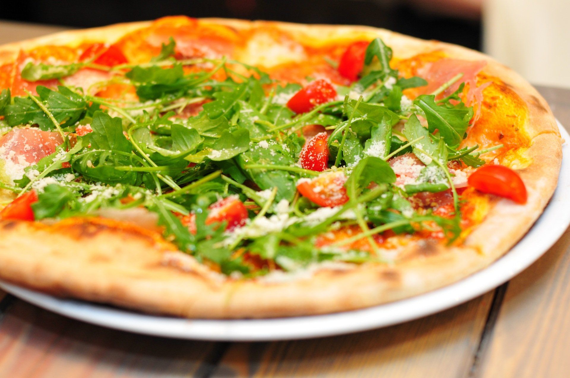 Pizza topped with arugula, tomatoes, and cheese on a white plate.
