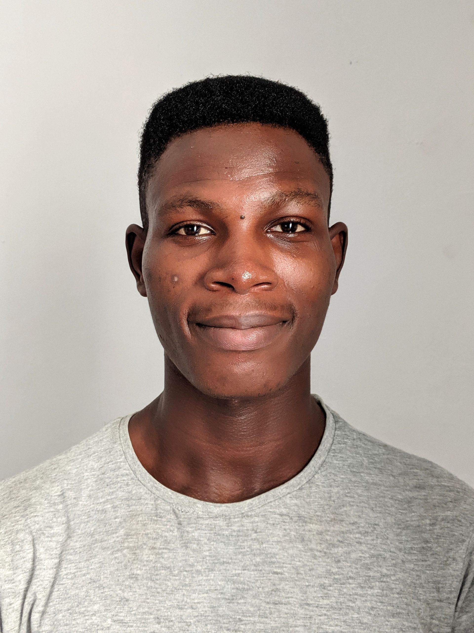 A young man in a grey shirt is smiling for the camera.