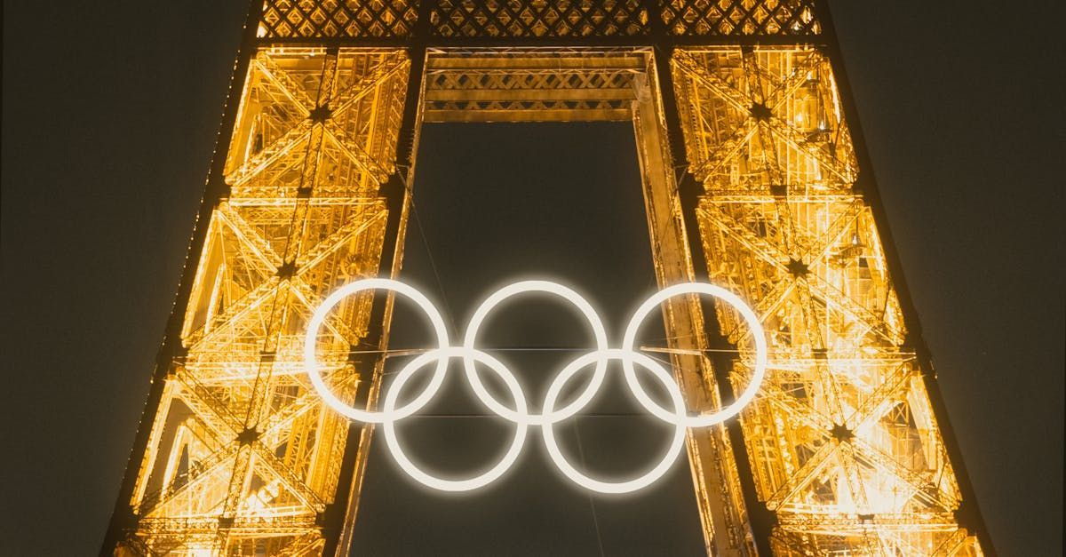 The eiffel tower is lit up at night with the olympic rings on it.