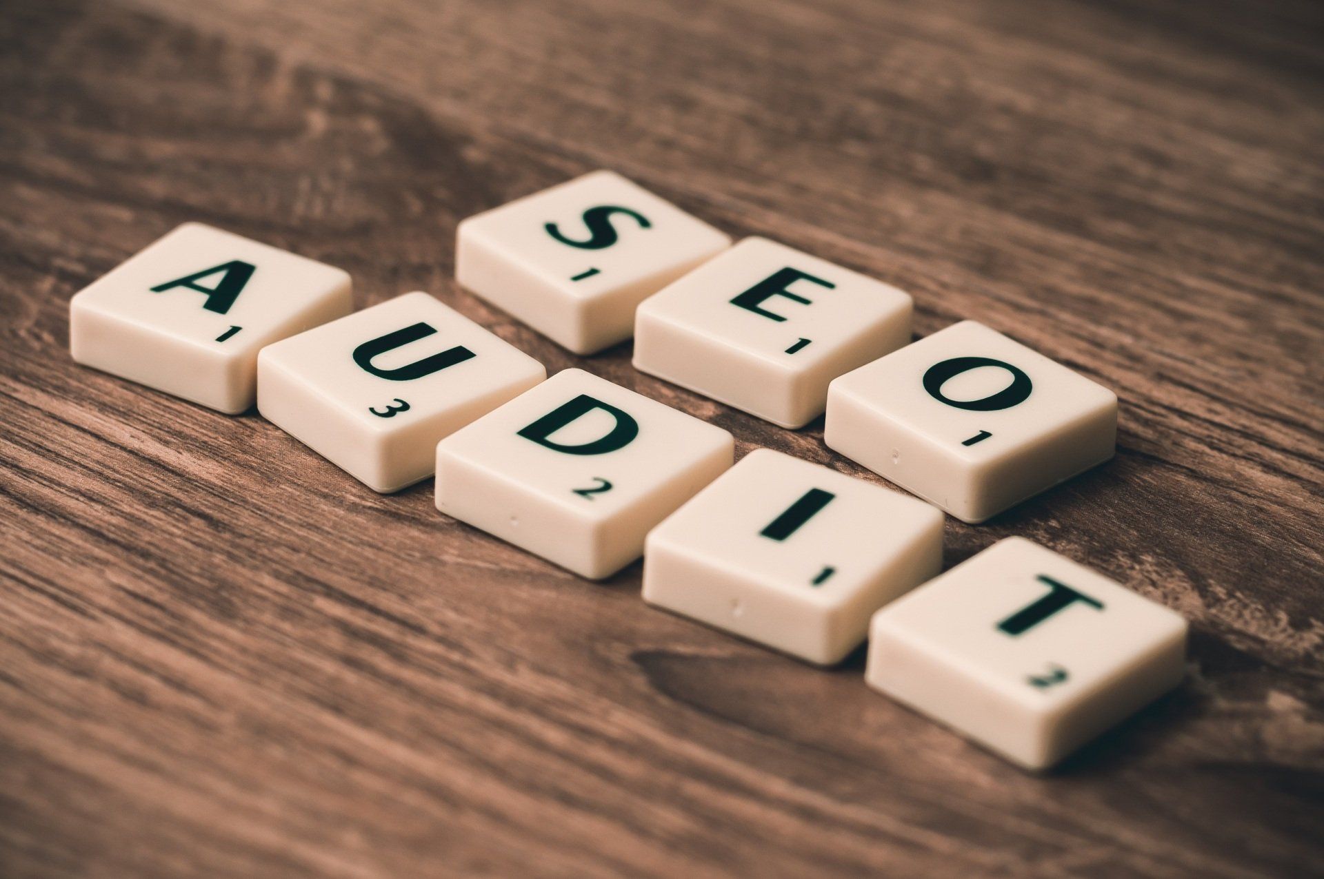 Scrabble tiles on a wooden table that spell out audit seo and audit