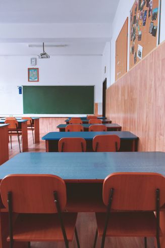 A classroom with tables and chairs and a green board
