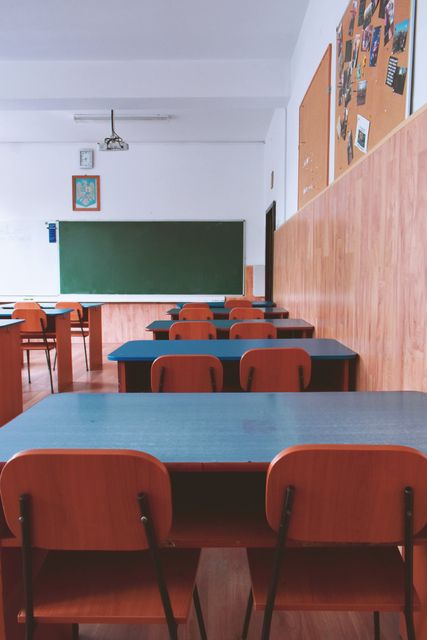 A classroom with tables and chairs and a green board