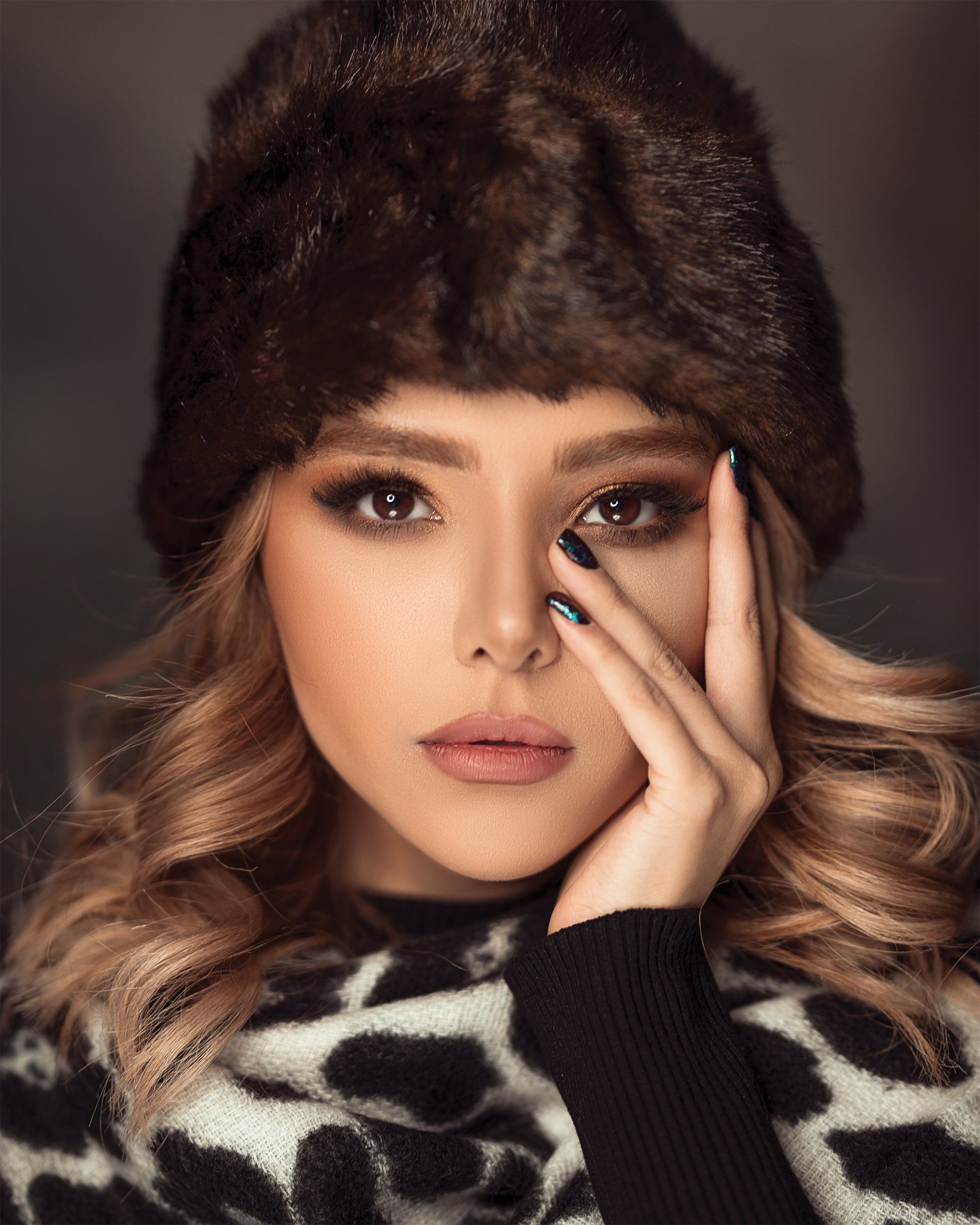 A woman wearing a fur hat and a leopard print sweater is covering her face with her hand.