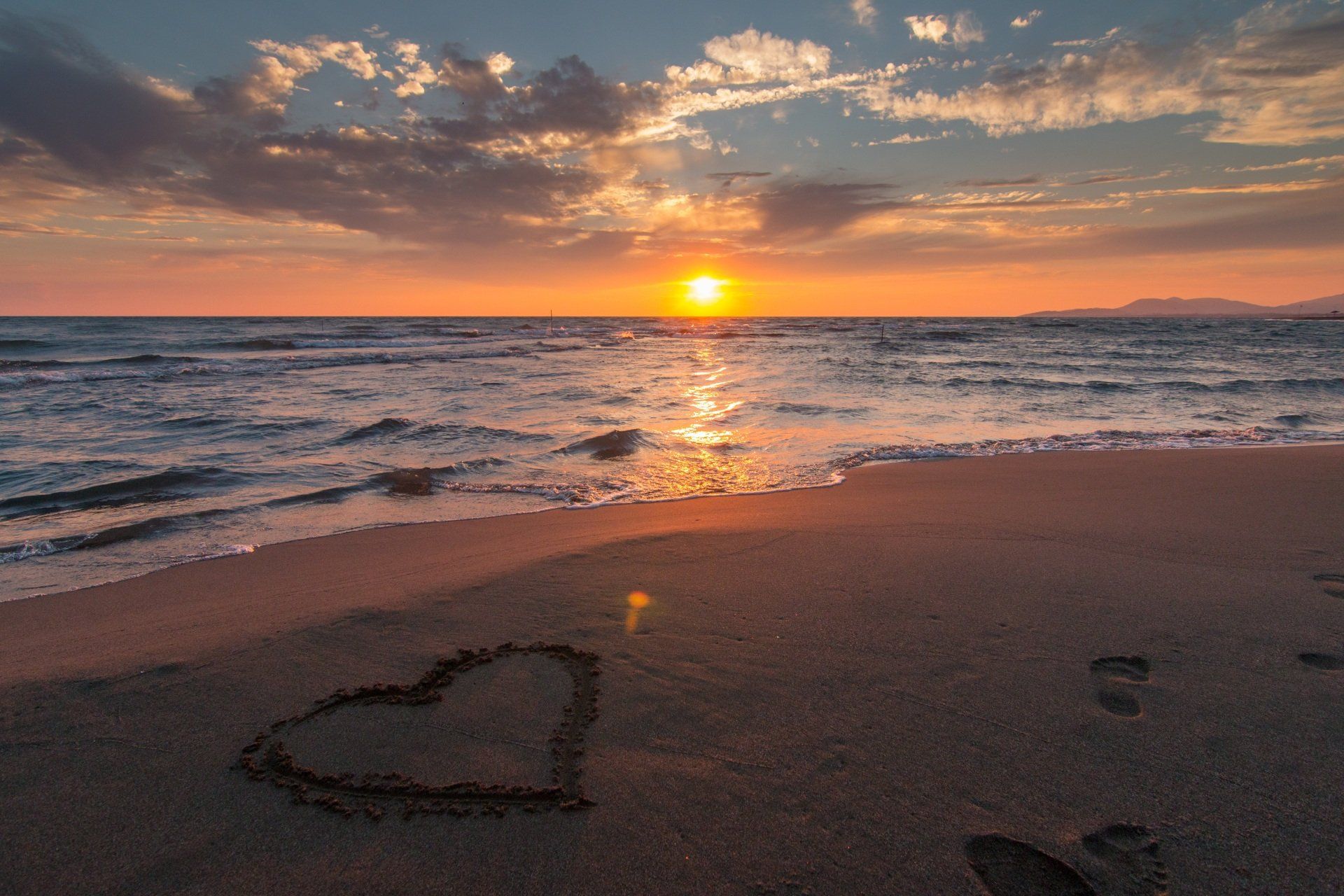 Um coração é desenhado na areia da praia ao pôr do sol.