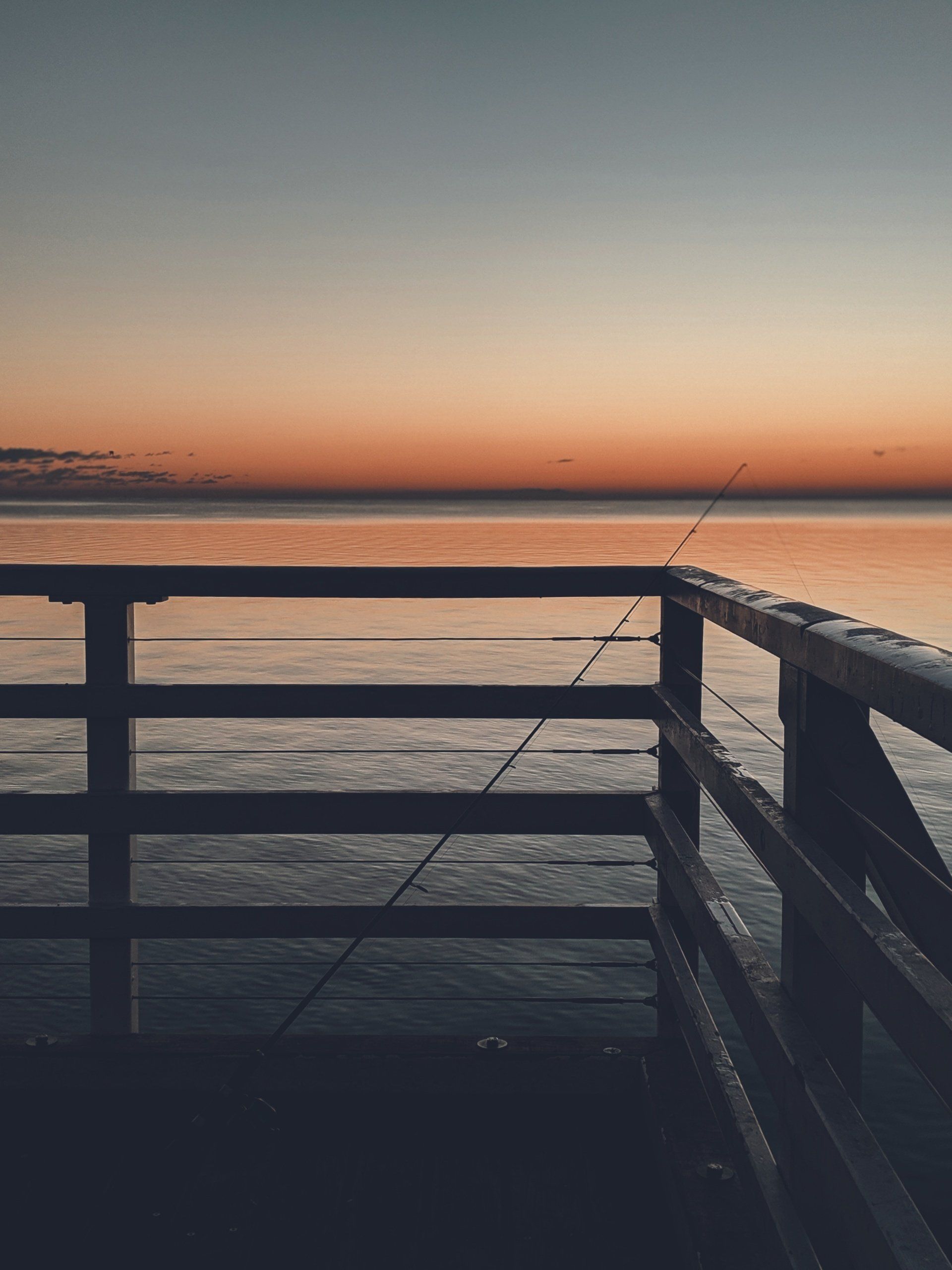 A pier with a fishing rod on it overlooking the ocean at sunset.