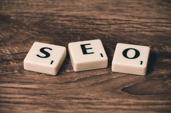 The word seo is written on scrabble tiles on a wooden table.