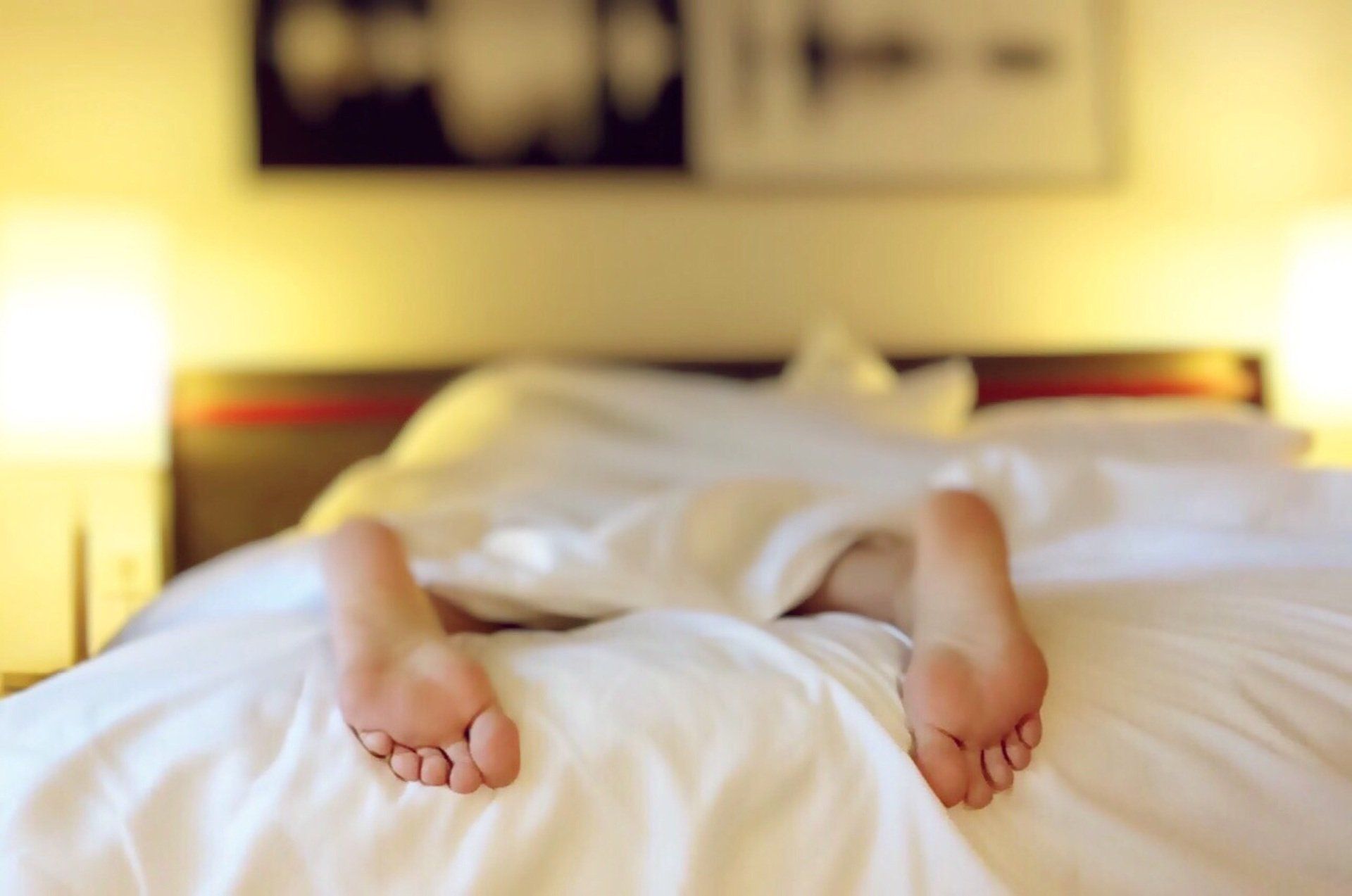 A person is laying in bed with their feet sticking out of the blankets.