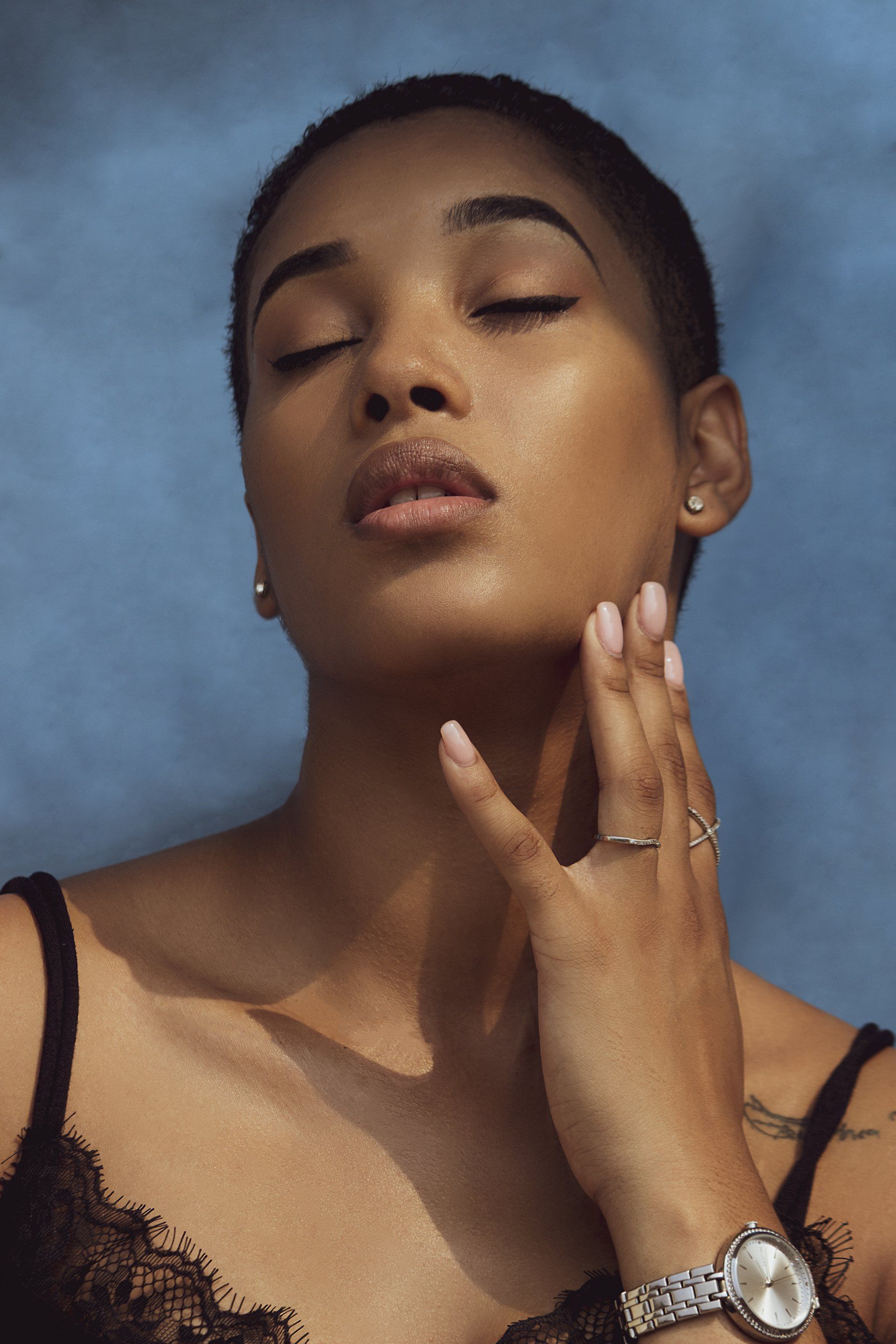 A woman wearing a watch and a ring is touching her face.