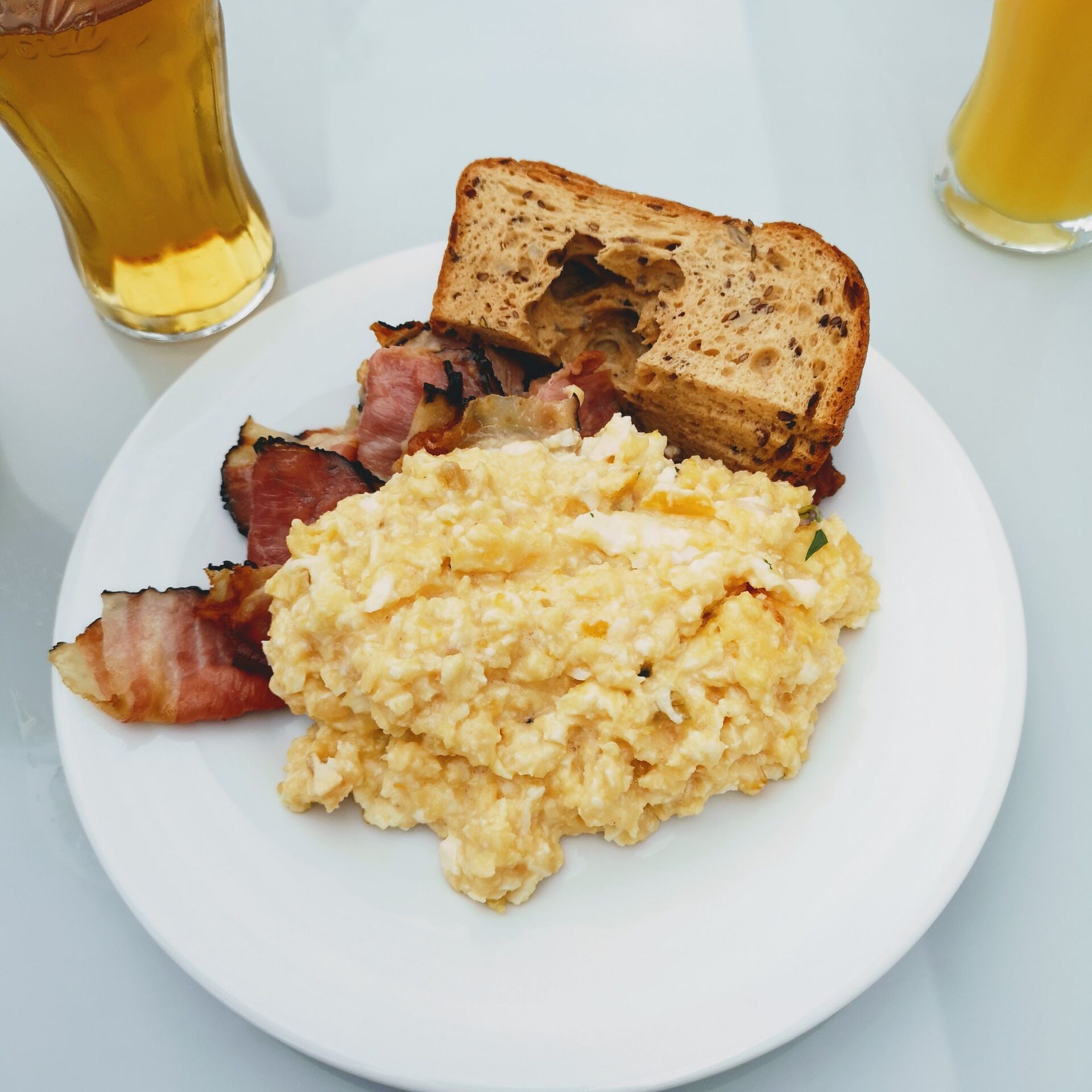 A white plate topped with scrambled eggs bacon and bread