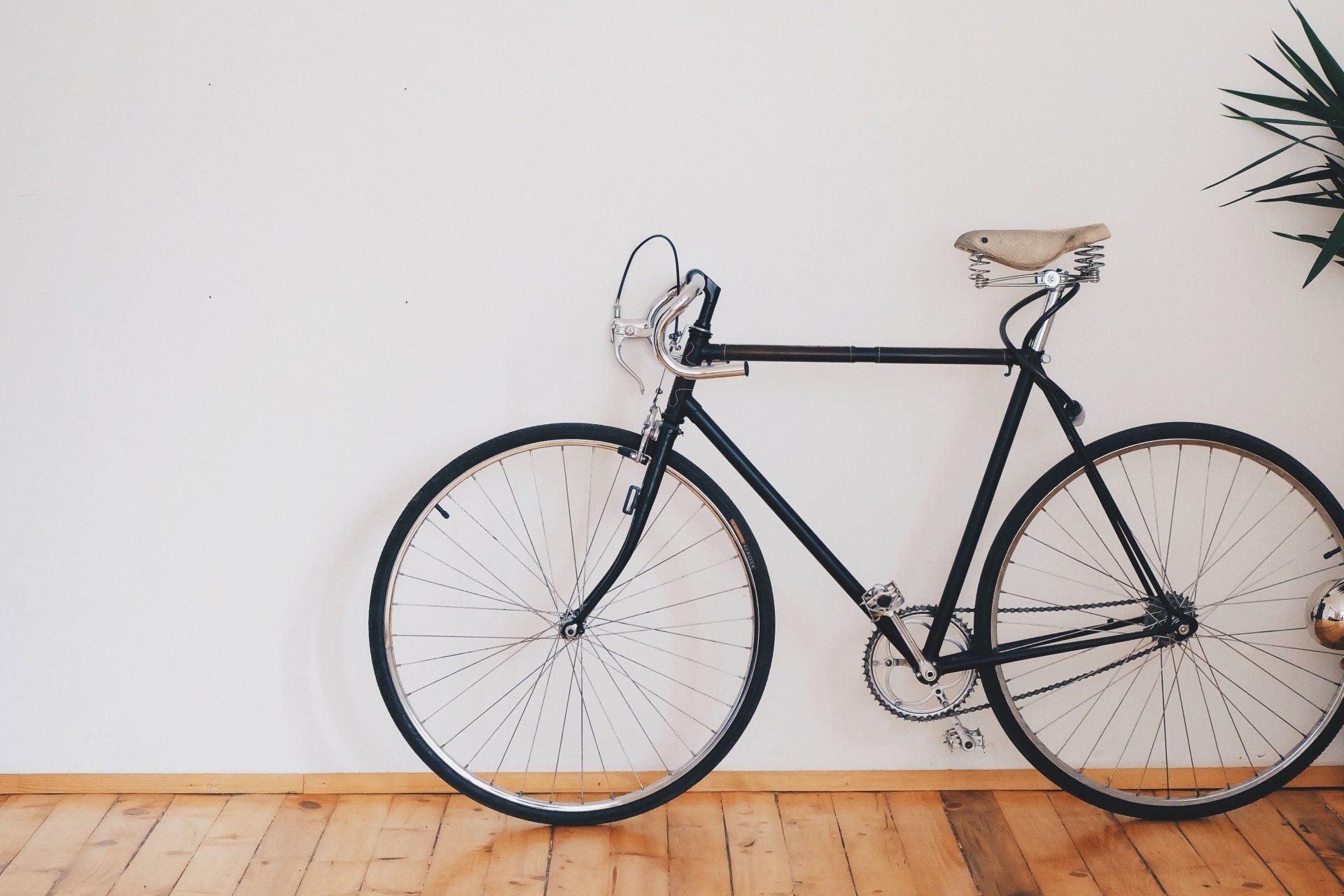 A black bicycle is leaning against a white wall