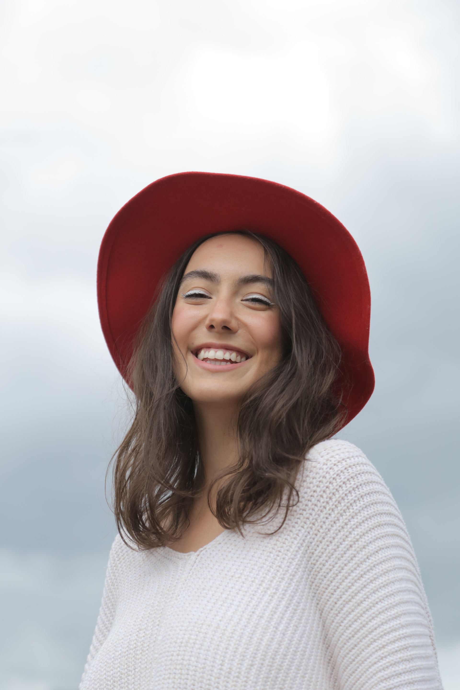 A woman wearing a red hat and a white sweater is smiling.