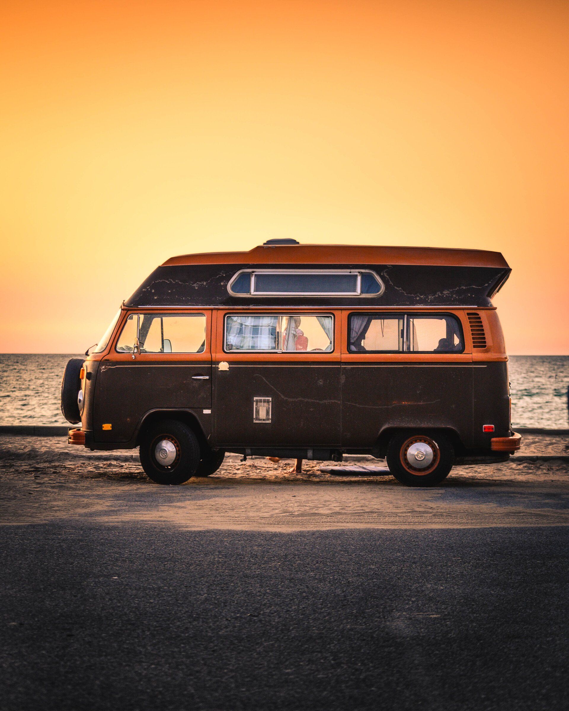 a brown and orange van is parked on the side of the road near the ocean .
