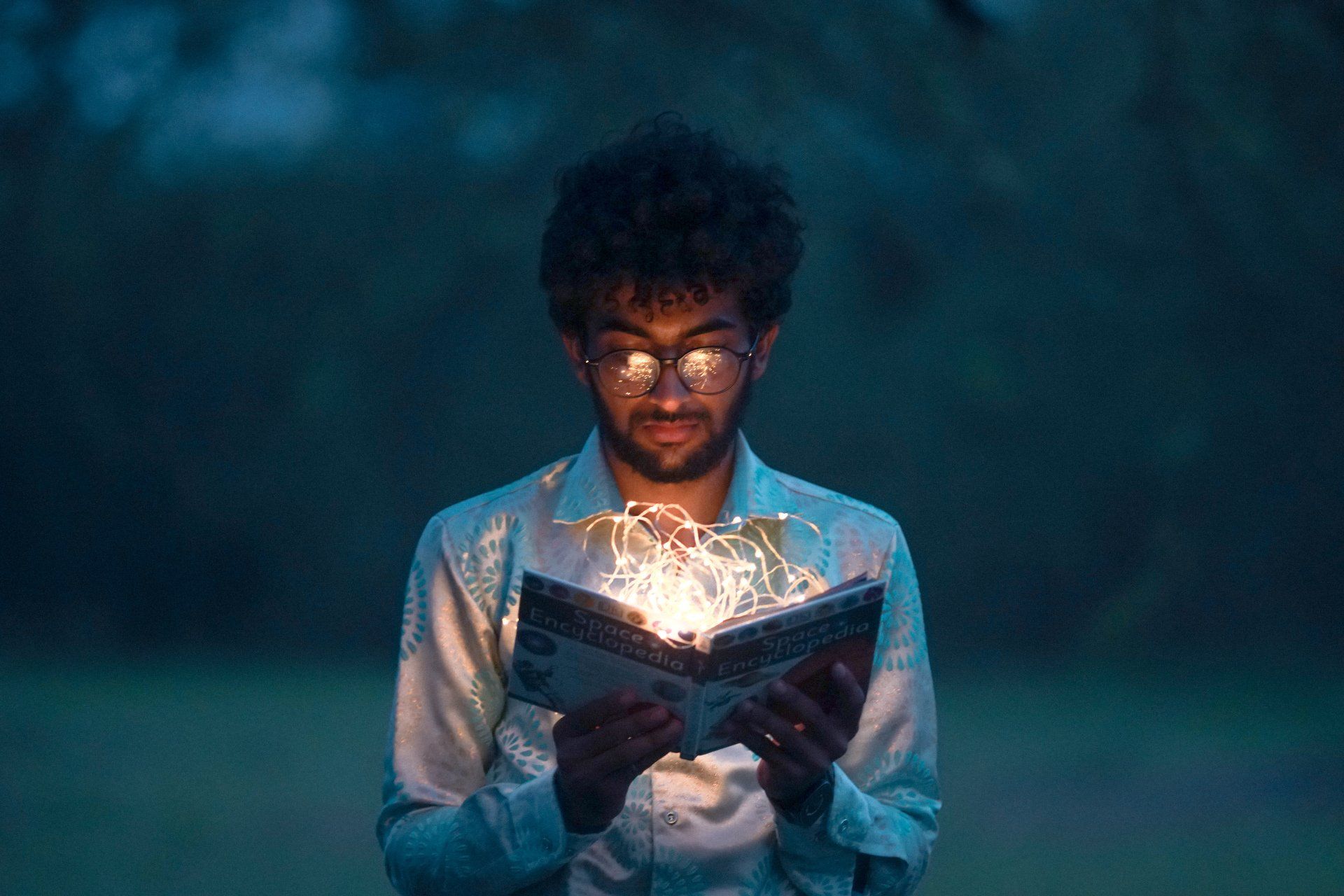 a man is reading a book with lights coming out of it .