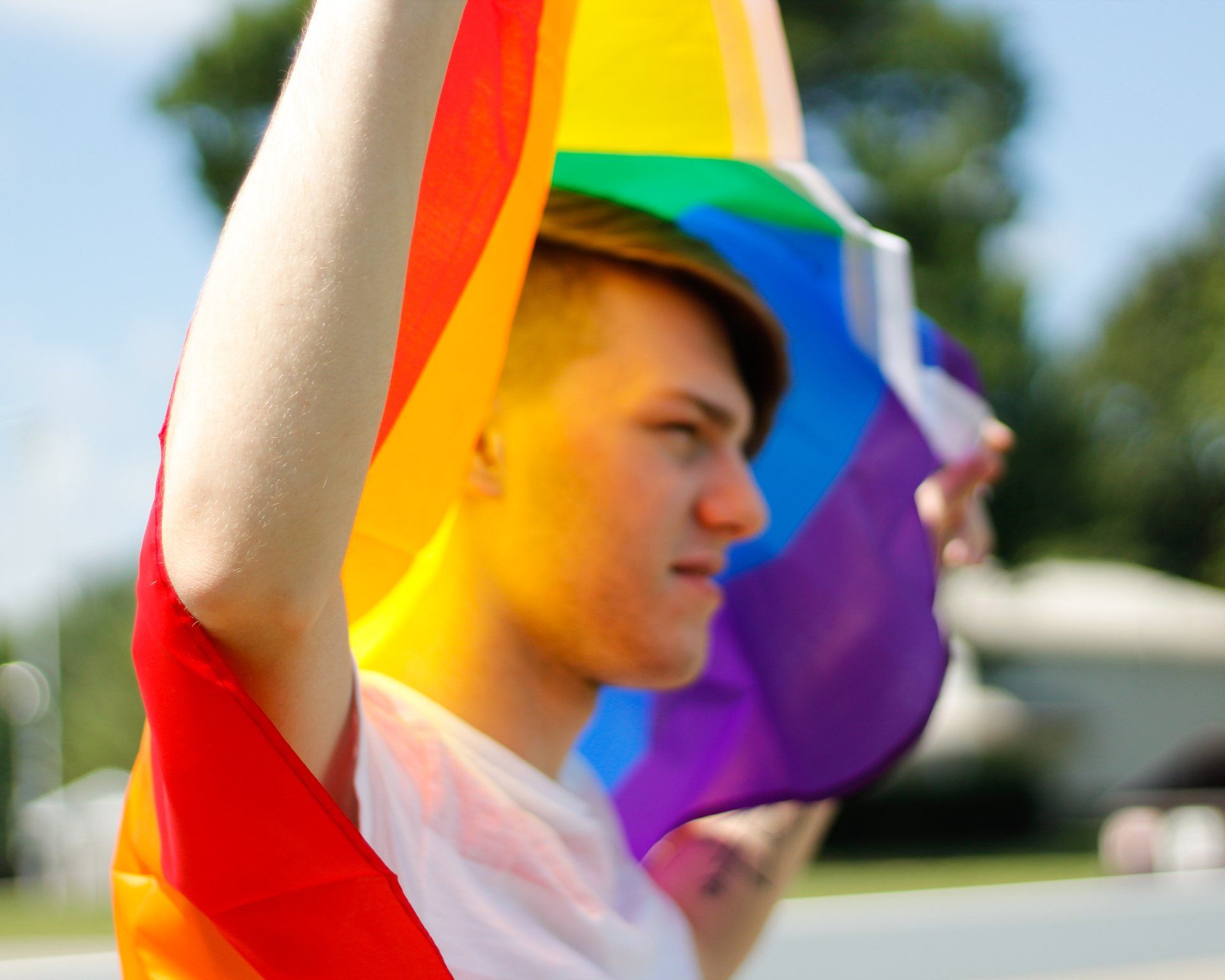 A young man is holding a rainbow flag over his head