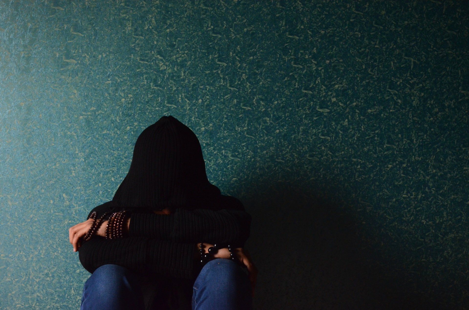 A person in a hoodie is sitting on the floor with their head down.