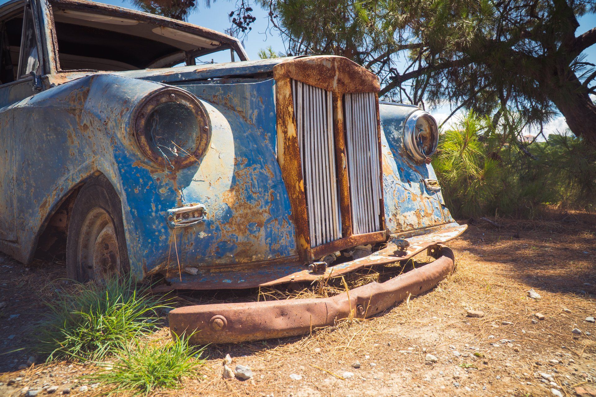 The front of a very old vehicle with the grill & bumper rusting out