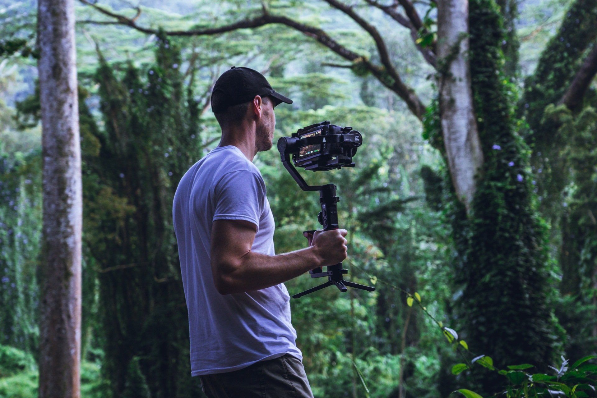 a man in a white shirt is holding a camera in a forest