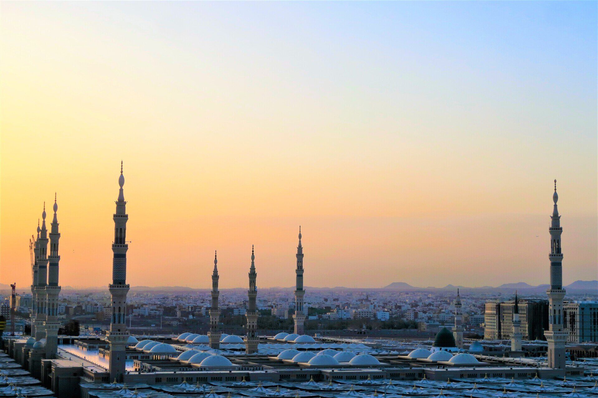 A cityscape with a mosque in the foreground and a sunset in the background.