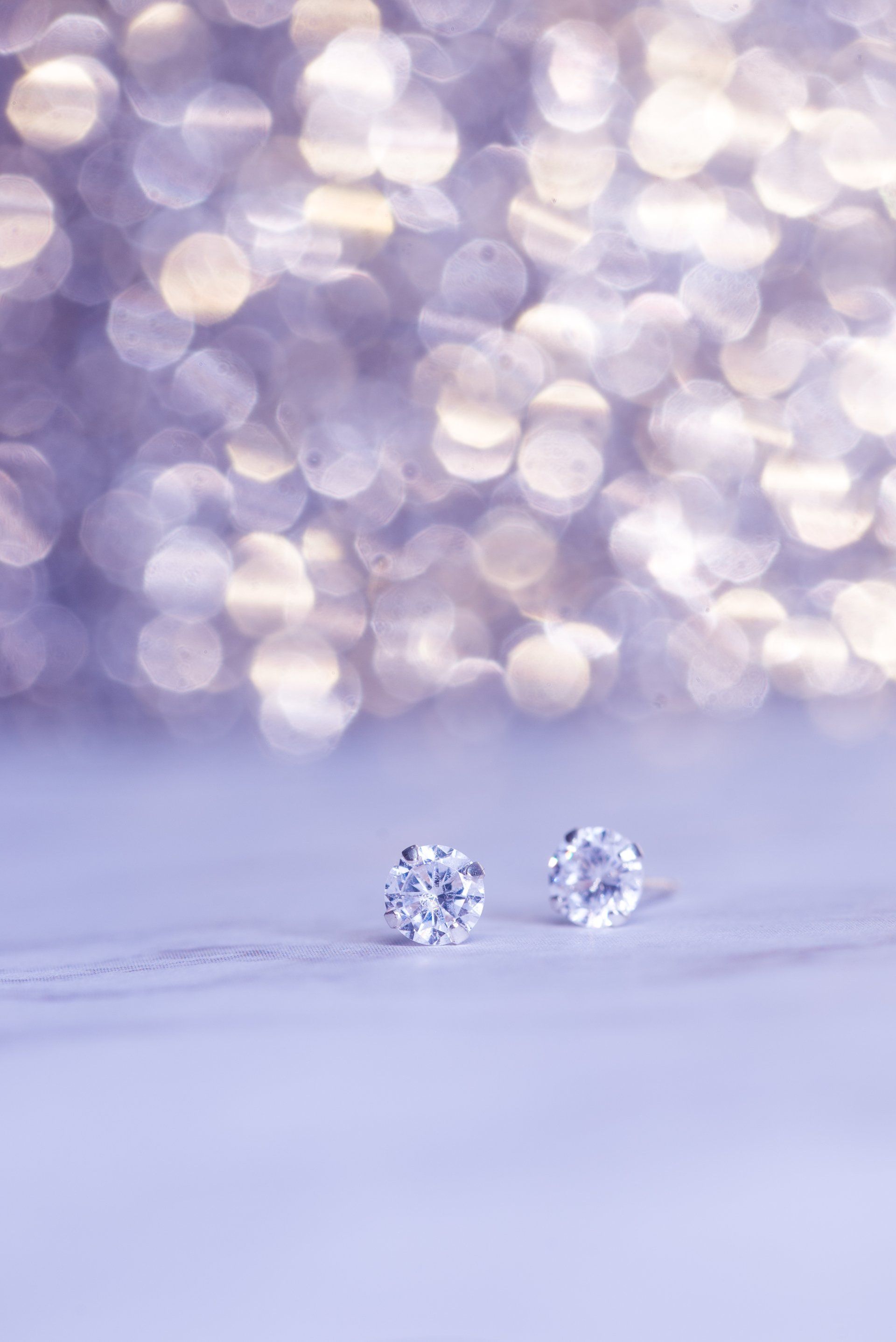 A pair of diamond stud earrings are sitting on a purple surface.