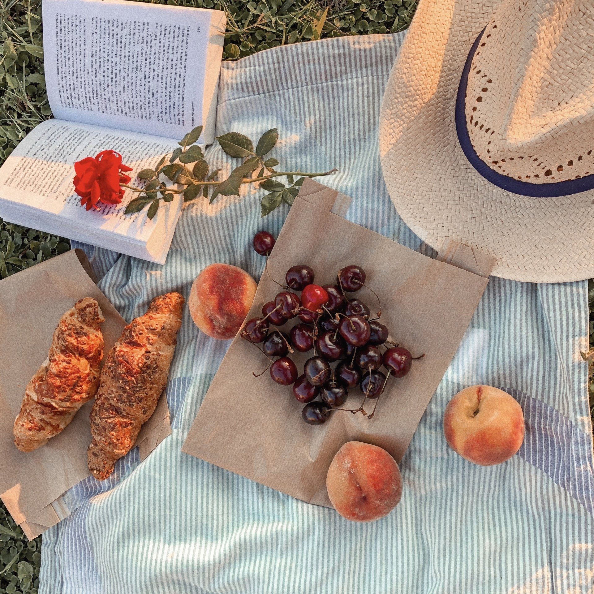 uma toalha de piquenique com croissants, cerejas, pêssegos e um chapéu