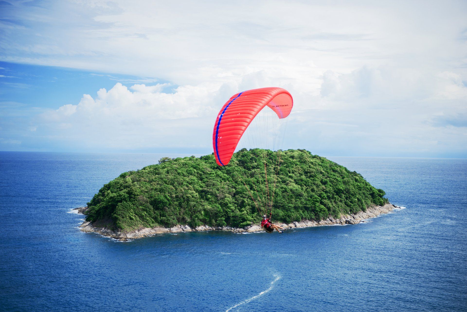 A person is parasailing over a small island in the middle of the ocean.