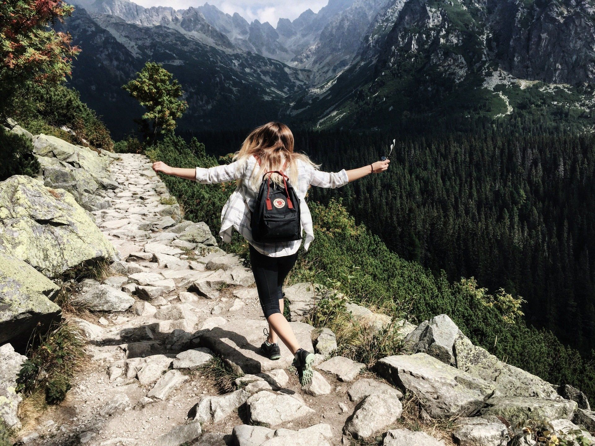 a woman with a backpack is walking on a rocky path in the mountains .
