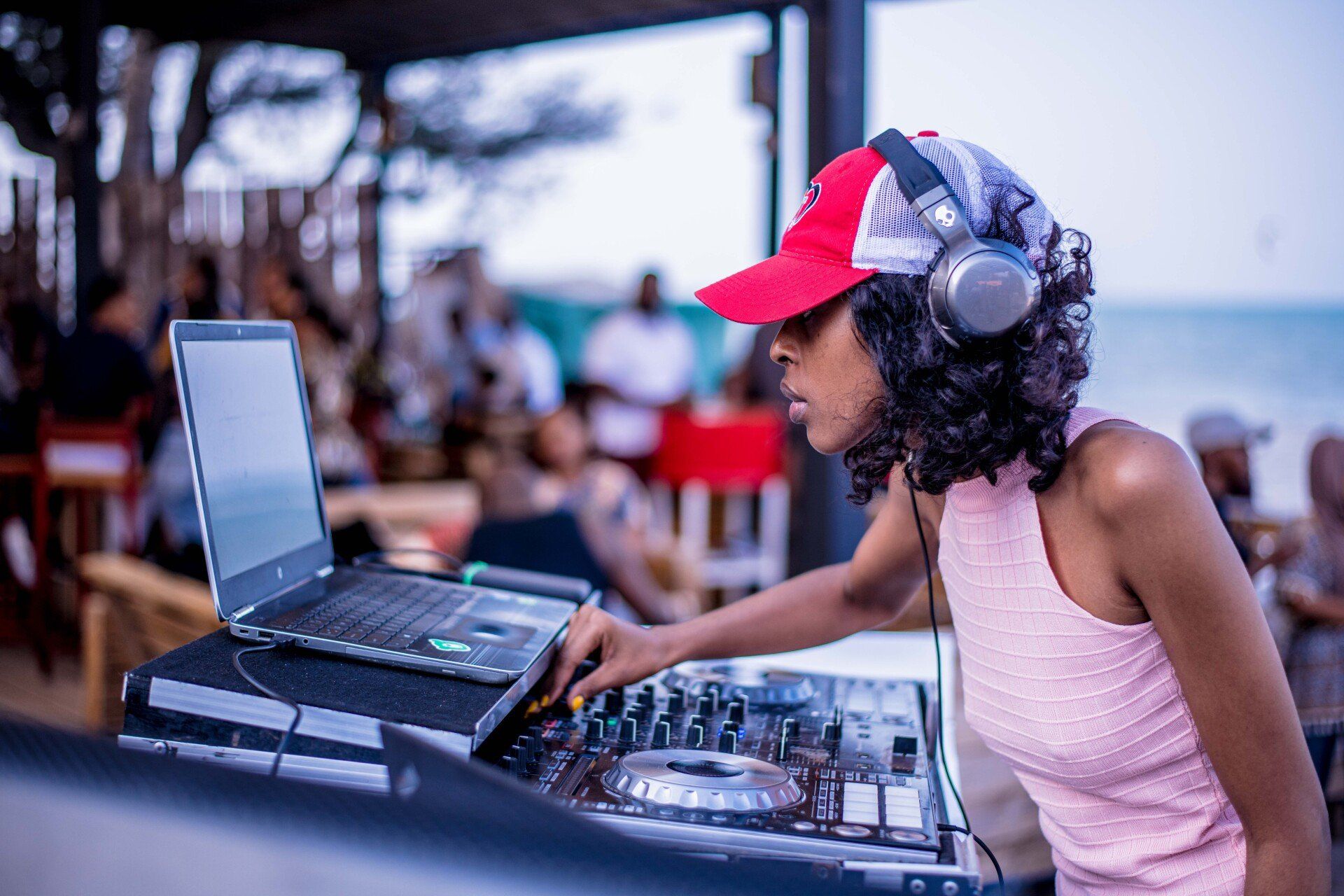 A woman wearing headphones and a red hat is playing music on a laptop.