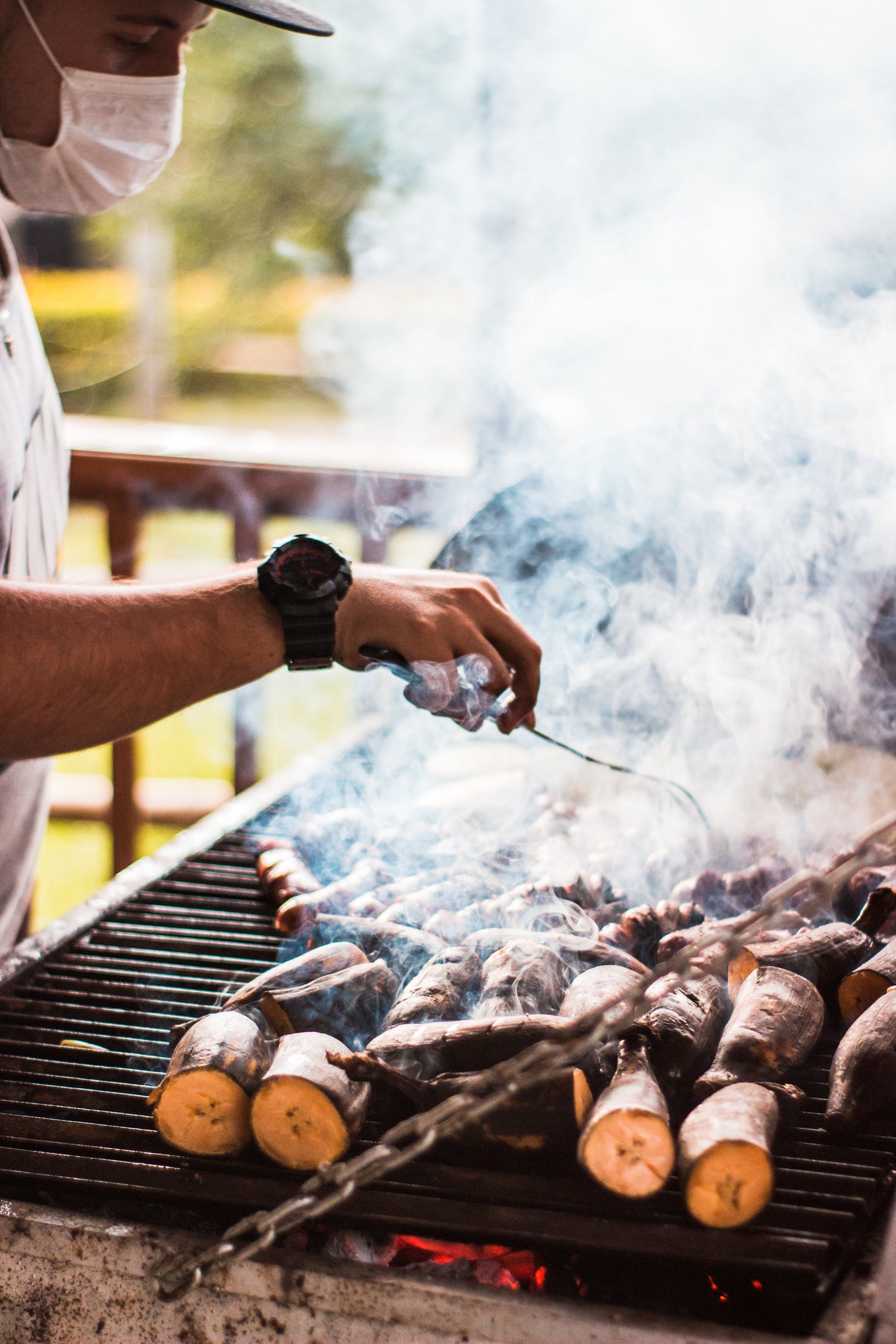 A man wearing a mask is cooking food on a grill.