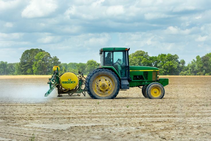 A green and yellow tractor is spraying a field.