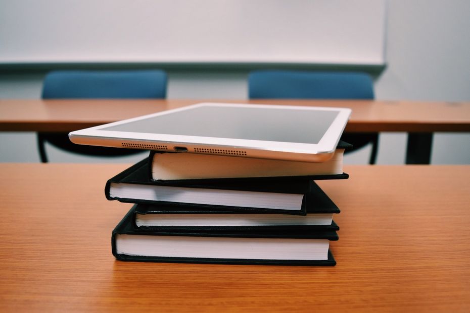 A tablet is sitting on top of a stack of books on a table.
