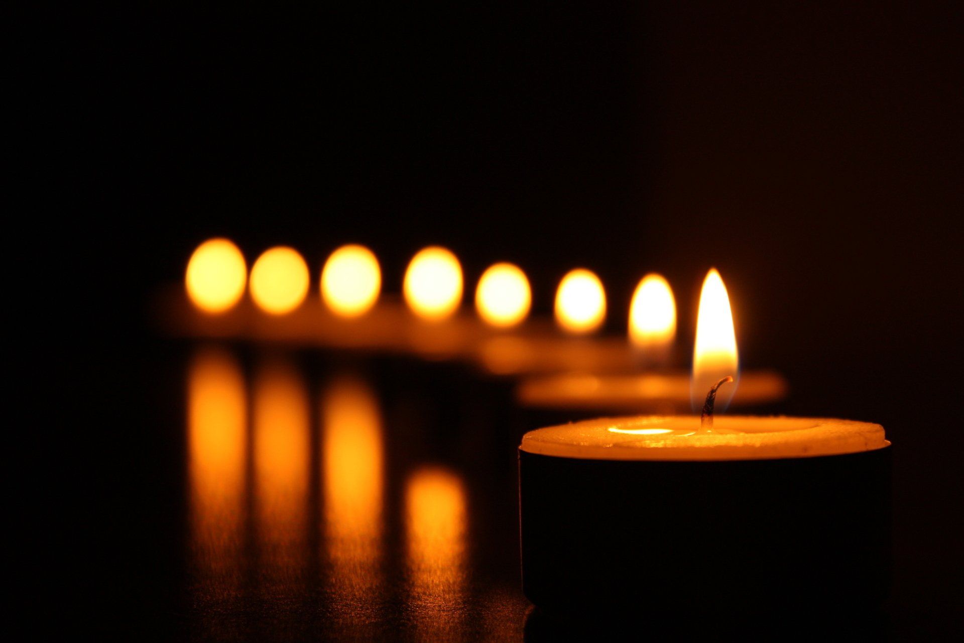 A row of lit candles in a dark room. Set to mourn someone after death.