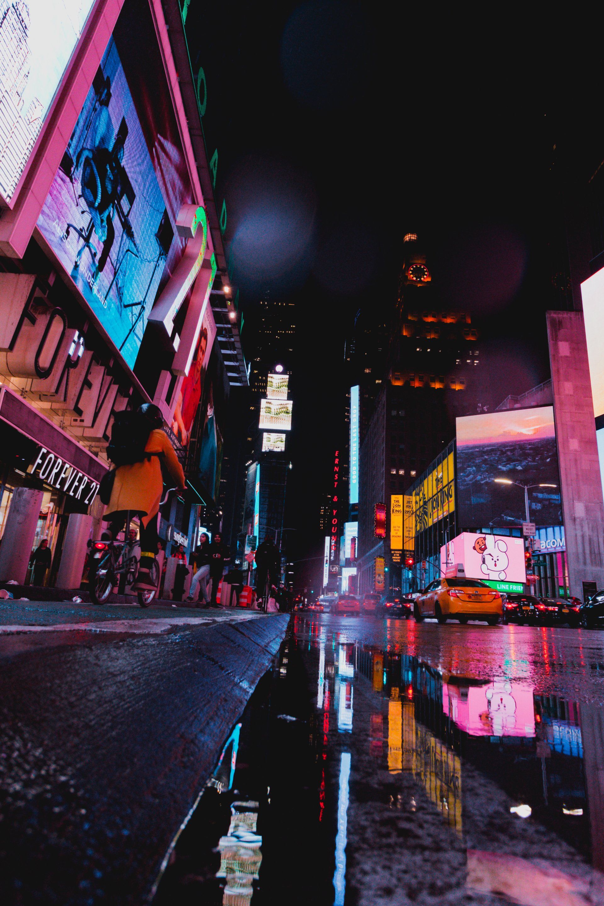 A city street at night with a reflection of buildings in a puddle.