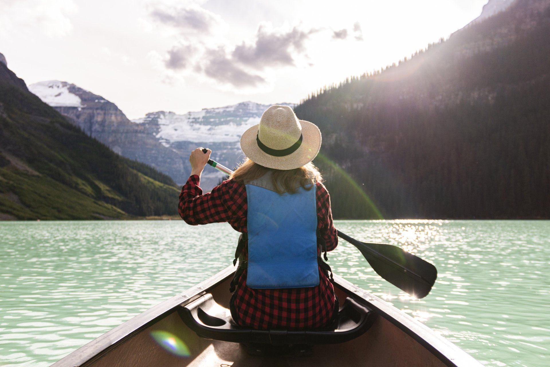 A woman in a hat is paddling a canoe on a lake.