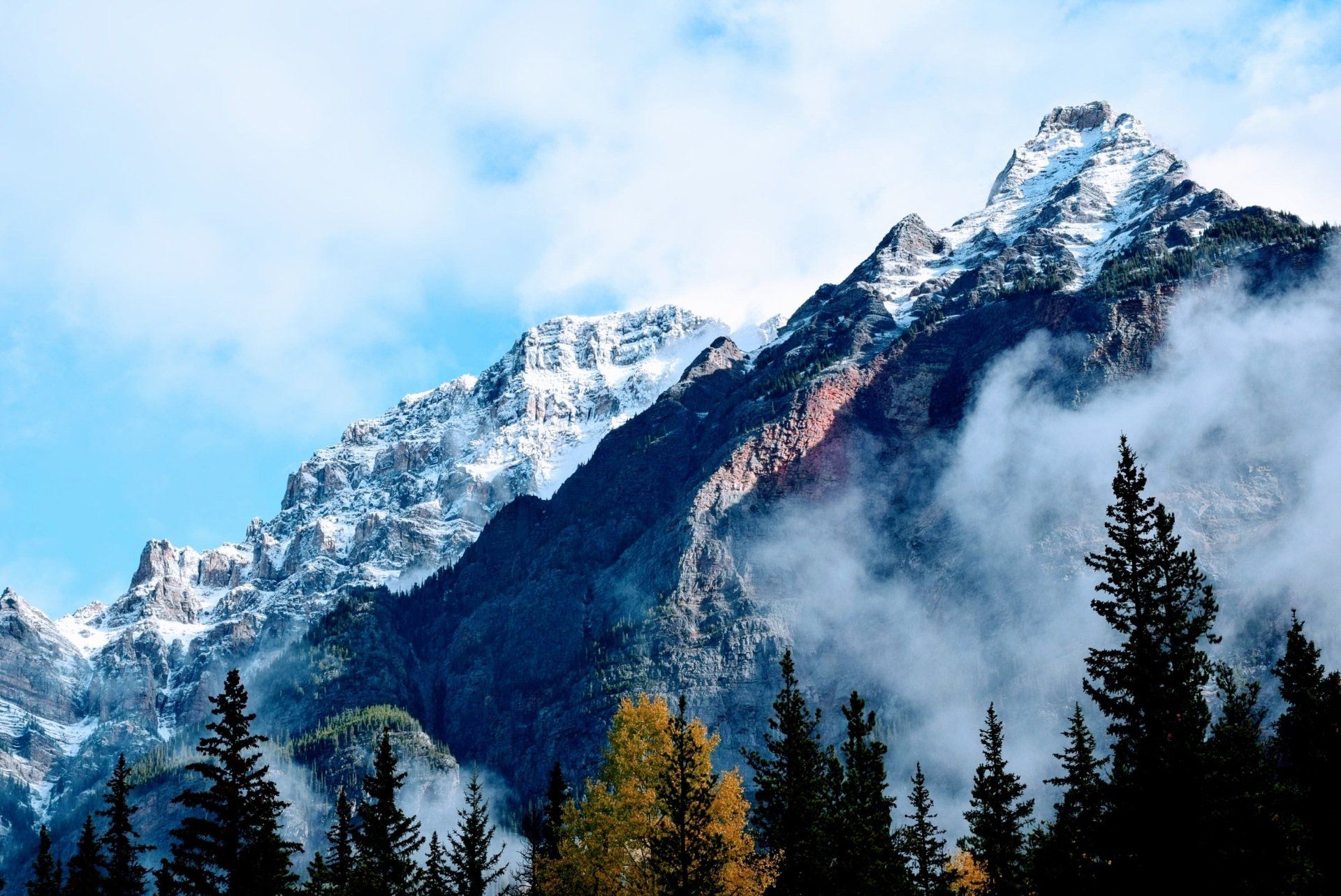 Ein schneebedeckter Berg mit Wolken und Bäumen im Vordergrund