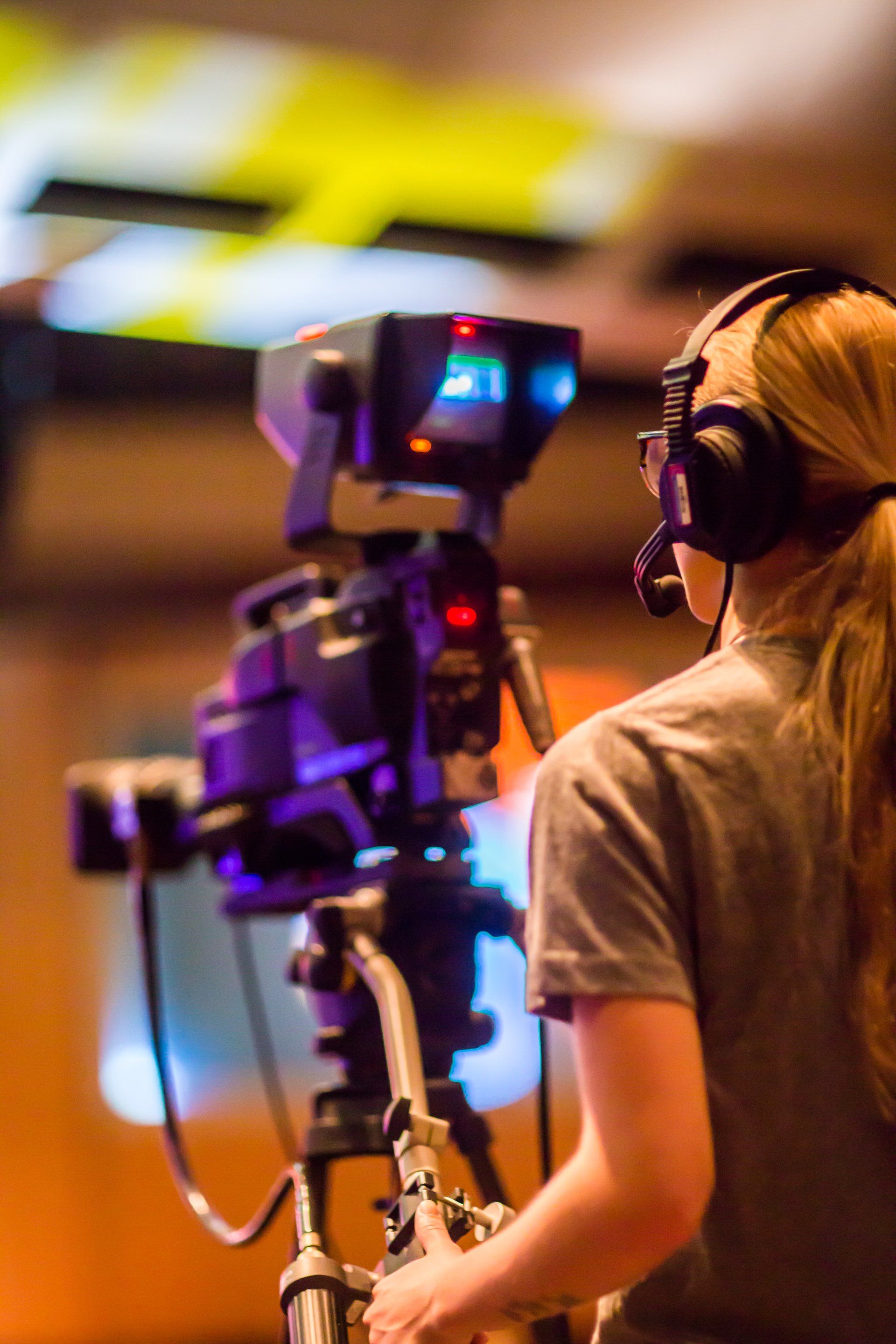 A woman wearing headphones is standing in front of a camera. filming sports. 