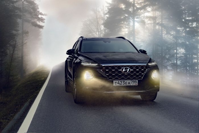 A black car is driving down a foggy road.
