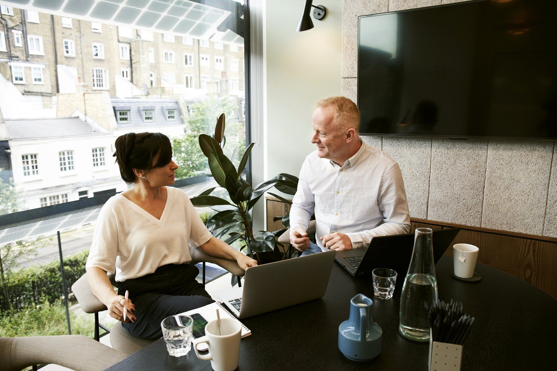 A man and a woman are sitting at a table with laptops.