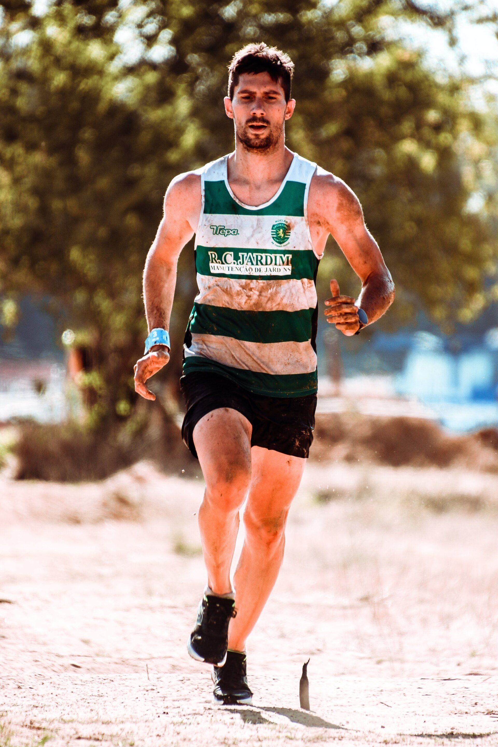 A man in a green and white tank top and black shorts is running on a dirt road.