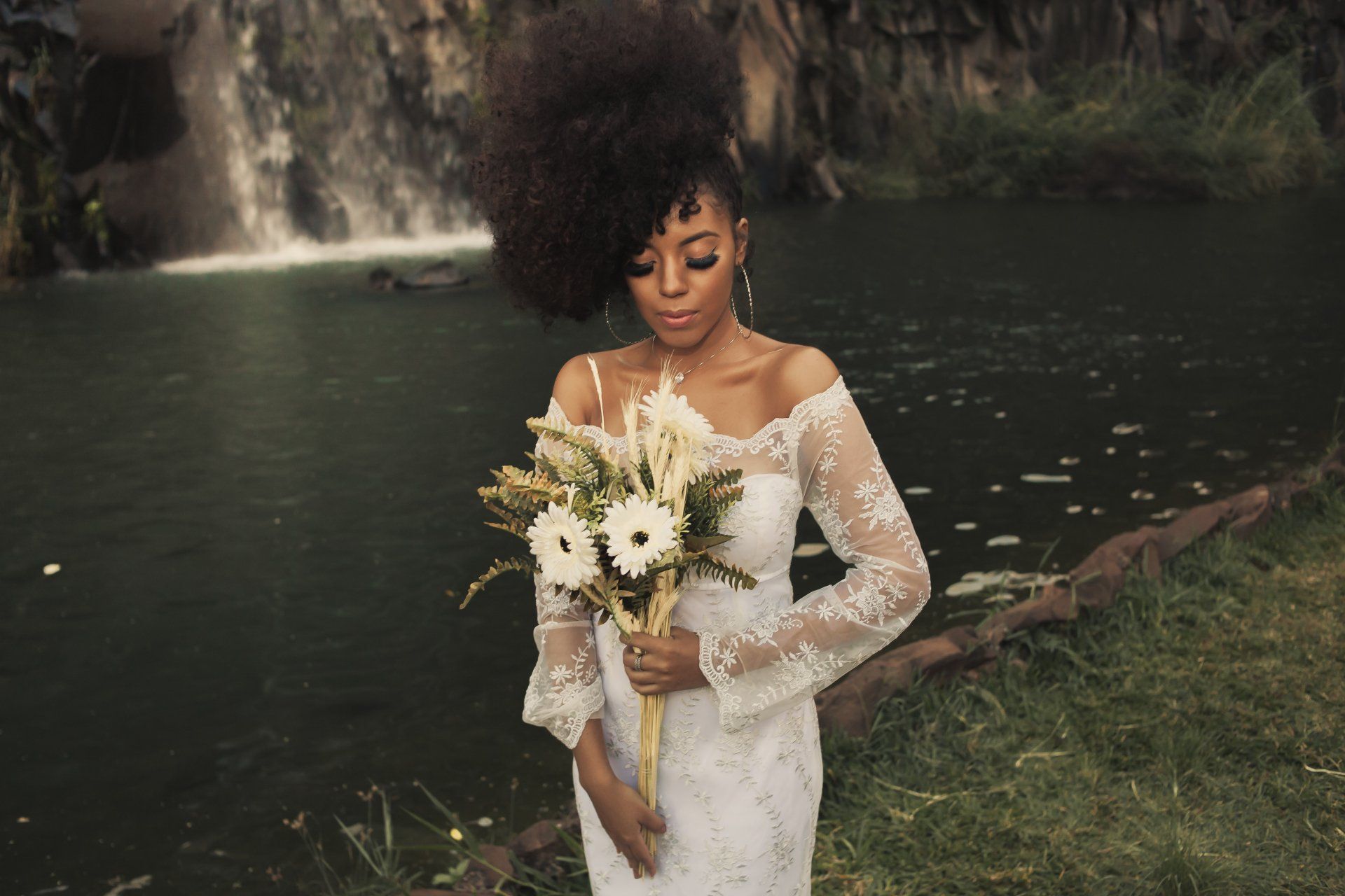 A woman in a wedding dress is holding a bouquet of flowers in front of a waterfall.
