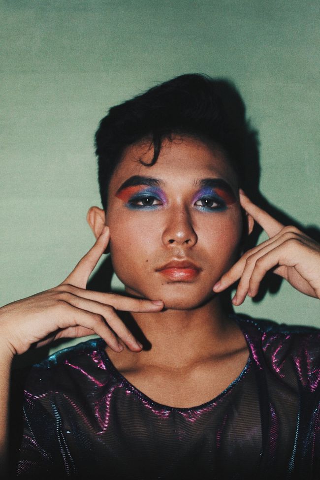 image of a young transgender individual wearing fun eye makeup and holding their face in their hands