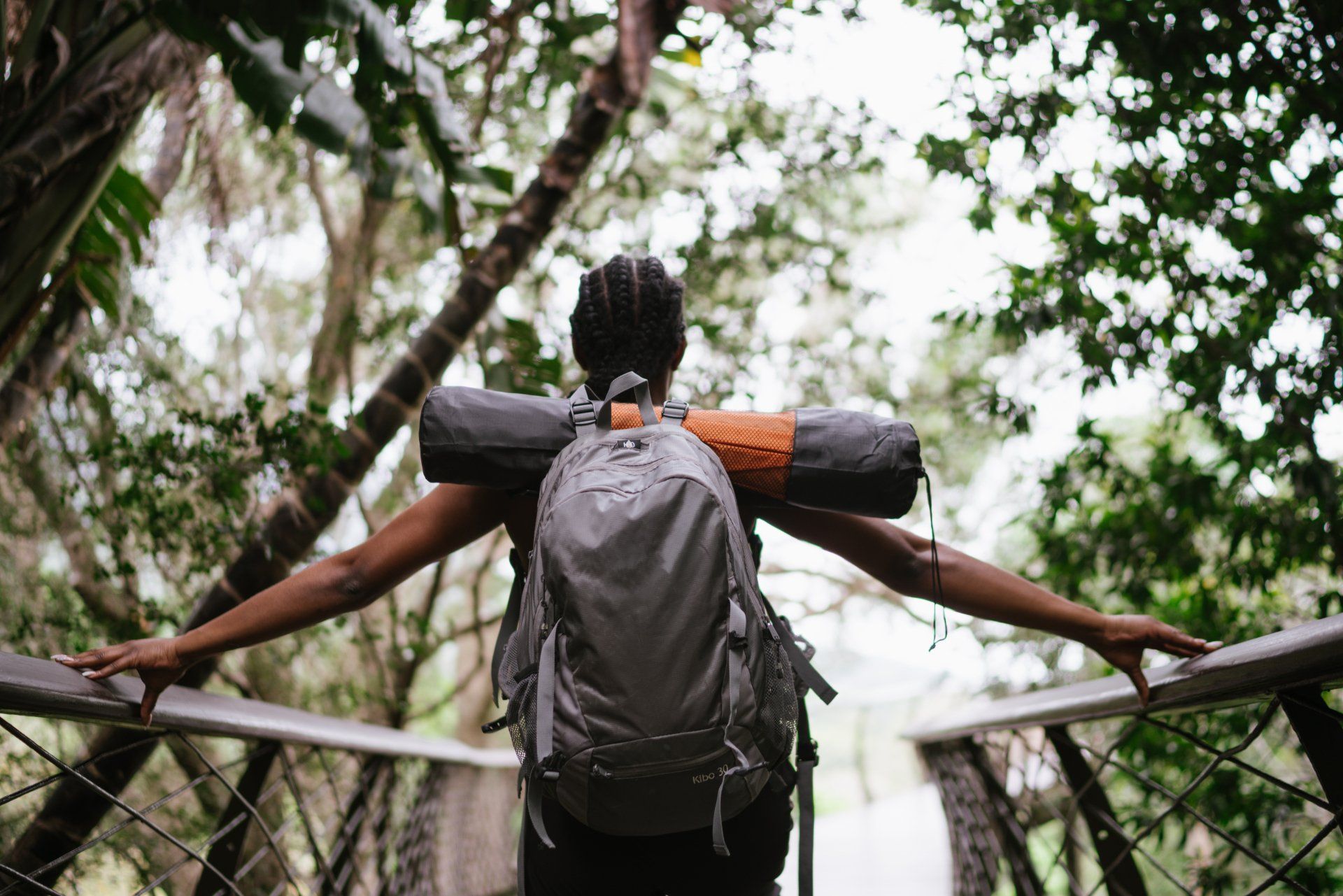 A woman with a backpack is standing on a bridge in the woods.
