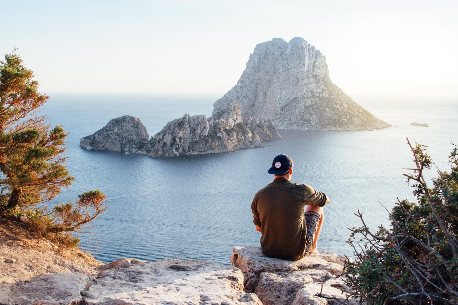 A man is sitting on top of a rock overlooking the ocean.