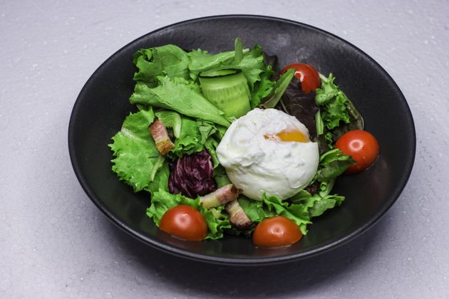 A salad with eggs , lettuce , tomatoes and bacon on a black plate.