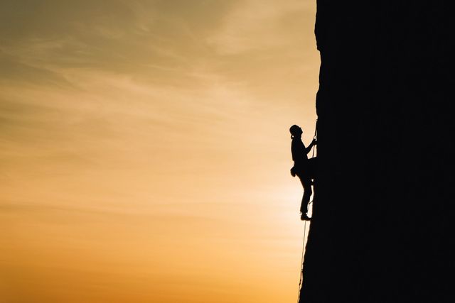 A silhouette of a person climbing a rock wall at sunset.