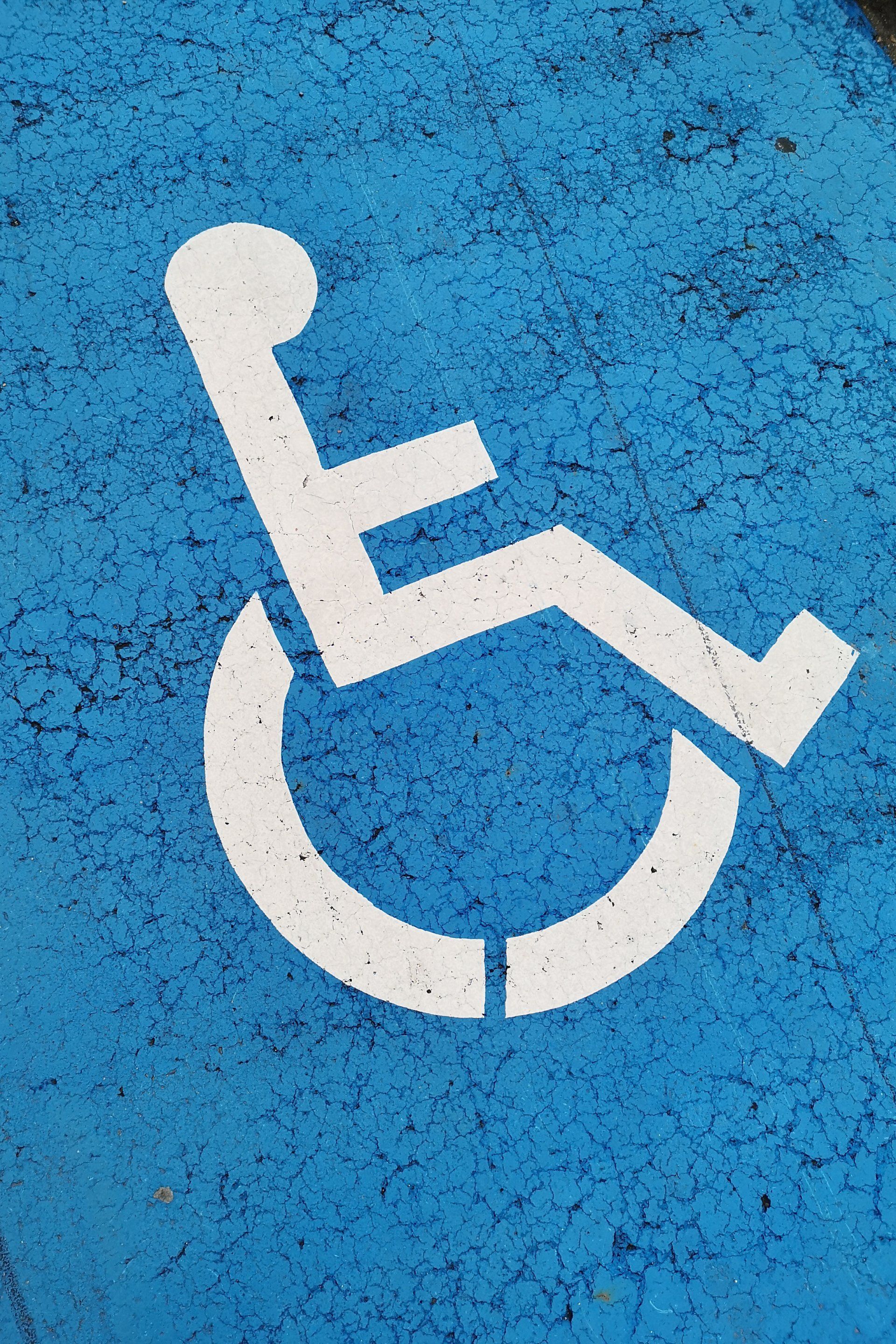 A white handicap sign is painted on a blue surface.