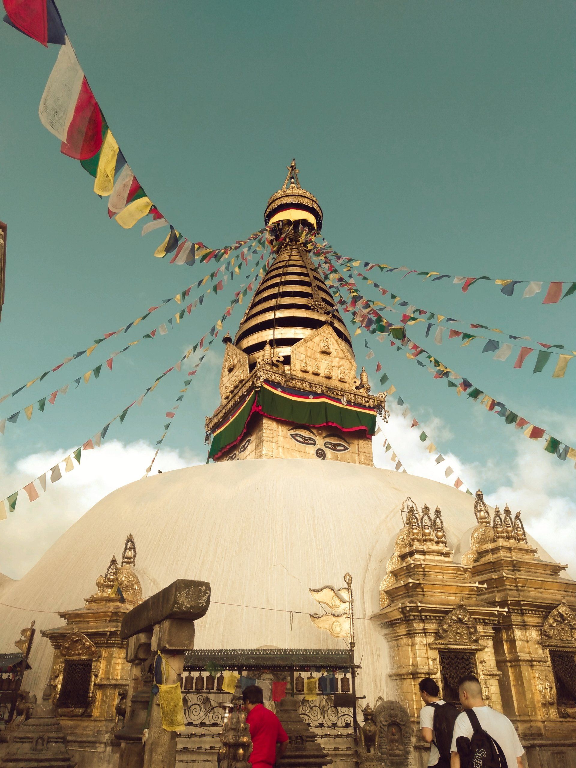 A group of people are standing in front of a temple with flags flying around it.