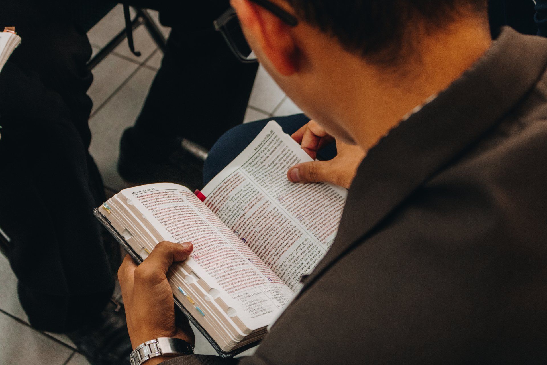 a man is sitting in a chair reading a bible .