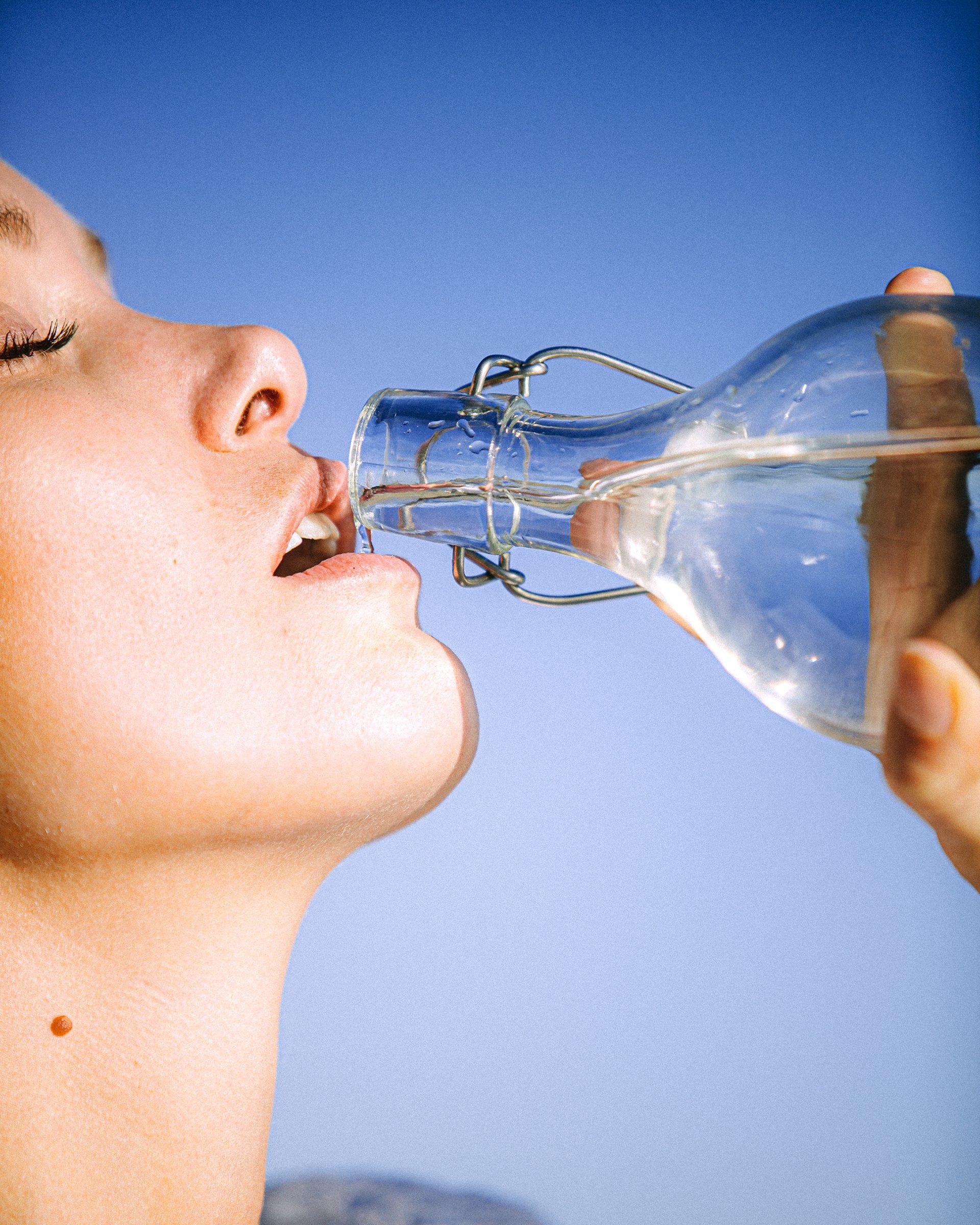 woman drinking water from a glass water bottle